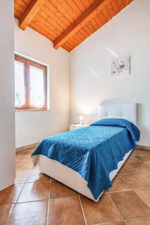 Une chambre à coucher avec un lit, une fenêtre, une table de chevet et une lampe fixée au mur.