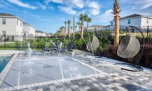 A water feature with fountains, a pool, and outdoor seating with a palm tree and fence in the background. - 11BR near Disney | Pool, spa & movie theater (Kissimmee)