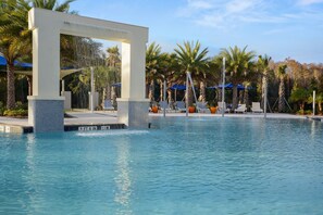 A swimming pool with a waterfall feature, lounge chairs, and palm trees. - 7BR near Disney | Private pool, spa & game room (Kissimmee)