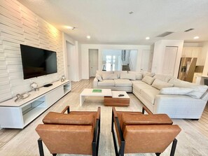 A modern living room with a sectional sofa, a flat-screen TV, a coffee table, and leather chairs. - 7BR near Disney | Private pool, spa & game room (Kissimmee)