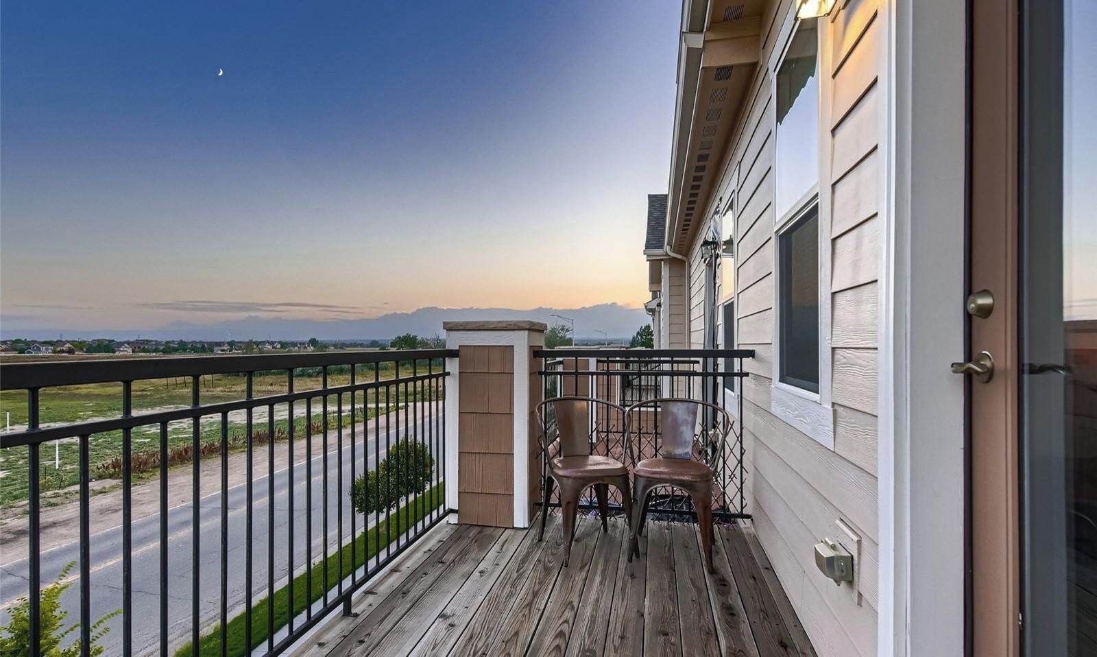 A balcony with a view of a road and distant mountains, a wooden deck, and two chairs.