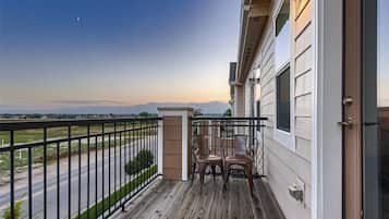 A balcony with a view of a road and distant mountains, a wooden deck, and two chairs.