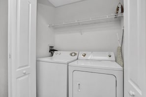 A laundry room with two washing machines and a dryer, a white door, and a shelf with a hanging rack. - 2BR condo near Disney | Resort pool (Kissimmee)