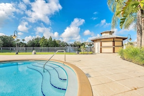 A swimming pool with a clear blue water feature, a small building with a brown roof, and a fenced area with trees and a clear sky. - 2BR condo near Disney | Resort pool (Kissimmee)
