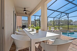 An outdoor patio with a table and chairs, a grill, and a view of a swimming pool and lake. - 8BR near Disney | Private pool, spa & lake view (Kissimmee)