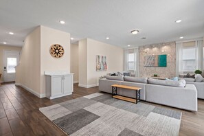 A modern living room with a sectional sofa, a coffee table, and a decorative wall piece. - 5BR near Disney | Pool, spa & game room (Kissimmee)