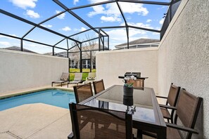 A pool area with a glass enclosure, a table with chairs, and a grill. - 5BR townhouse near Disney | Pool & Oasis Club (Davenport)