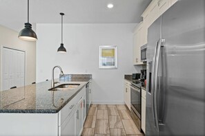 Eine moderne Küche mit einem Edelstahl-Kühlschrank, einer Spüle mit zwei Becken und einer Arbeitsplatte aus Granit.