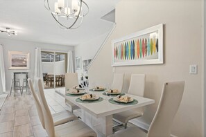 A dining area with a white table set for four, a chandelier, and a colorful abstract painting on the wall. - 5BR townhouse near Disney | Pool & Oasis Club (Davenport)