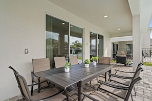 An outdoor patio with a rectangular table and six chairs, a grill, and potted plants. - 6BR near Disney | Private pool & game room (Kissimmee)