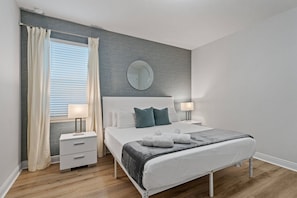 Un dormitorio moderno con una cama, mesitas de noche, un espejo y una ventana con cortinas.