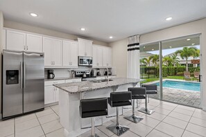 A modern kitchen with white cabinets, stainless steel appliances, and a granite countertop. - 6BR near Disney | Private pool & game room (Kissimmee)