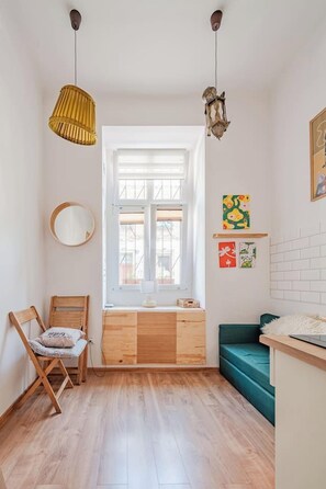 Ein Zimmer mit Fenster, einem Holztisch, einem grünen Sofa, einem Sessel und Wandbildern.