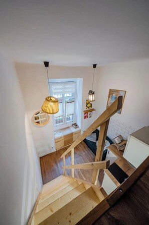 Eine Holztreppe mit Handlauf, eine hängende Pendelleuchte und ein Fenster mit Ausblick.