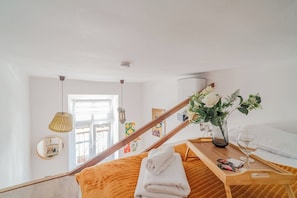 A hotel room with a wooden staircase, a wooden bed, a bedside table with a vase and a glass, and a window with blinds. - Kraków City Center Studio — Mezzanine (Kraków)