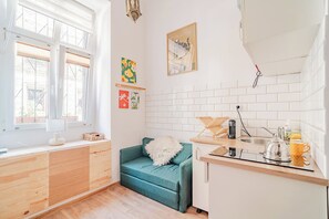A compact kitchen with a window, a teal sofa, and a white tiled backsplash. - Kraków City Center Studio — Mezzanine (Kraków)
