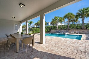 Un patio cubierto con piscina, mobiliario exterior y vistas al vecindario.