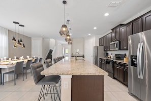 A modern kitchen with a central island, stainless steel appliances, and pendant lighting. - 10BR near Disney | Private pool, spa & game room (Kissimmee)