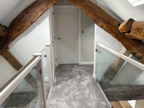 Eine schmale Treppe mit Glasgeländern führt zu einer Tür, umgeben von freiliegenden Holzbalken.