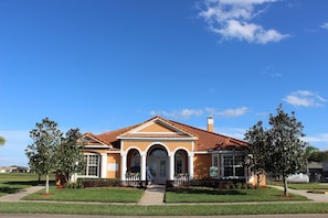 A two-story house with a brown facade, a red-tiled roof, and a front porch with a covered bench. - 4BR home in Kissimmee | Mickey & Minnie room (Kissimmee)