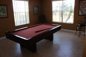 A pool table in a room with two windows, a chair, and a poster on the wall. - 4BR home in Kissimmee | Mickey & Minnie room (Kissimmee)