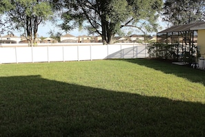 A residential area with a fenced yard, a house with a covered porch, and trees in the background. - 4BR home in Kissimmee | Mickey & Minnie room (Kissimmee)