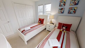 A bedroom with two single beds, a nightstand with a lamp, and a door. - 4BR home in Kissimmee | Mickey & Minnie room (Kissimmee)