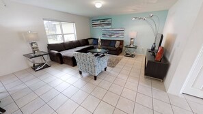 A living room with a sectional sofa, a patterned armchair, a coffee table, a side table, and a lamp. - 4BR home in Kissimmee | Mickey & Minnie room (Kissimmee)