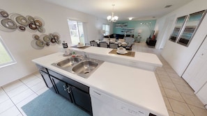 A modern kitchen with a double sink, a dishwasher, and a dining area with a table set for two. - 4BR home in Kissimmee | Mickey & Minnie room (Kissimmee)