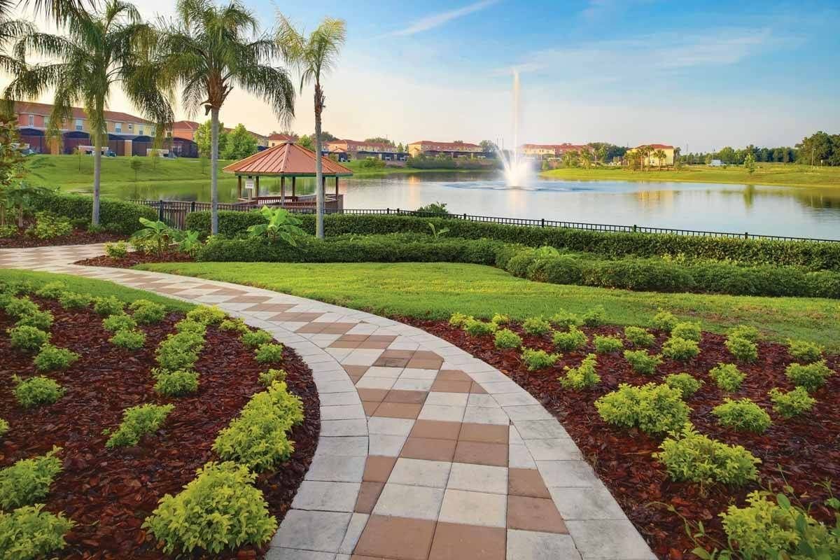 A landscaped pathway leading to a gazebo, a body of water, and a fountain.