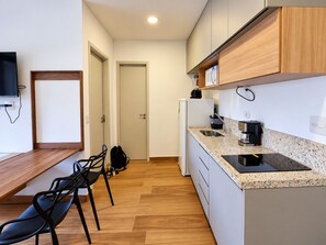 A compact kitchen with a microwave, coffee maker, and a small refrigerator. There is a dining area with chairs and a table. - Premium Studio 33 | Near Ibirapuera | iamspe (São Paulo)