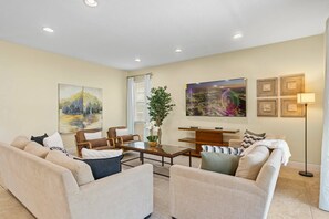 A living room with a sofa set, a coffee table, a TV, and a painting on the wall. - 5BR near Disney | Private pool, spa & game room (Kissimmee)