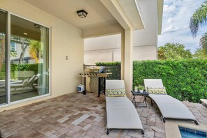 A covered patio area with a grill, lounge chairs, and a small table. - 5BR near Disney | Private pool, spa & game room (Kissimmee)