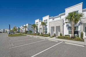 A row of modern, white buildings with stone accents, a parking lot, and palm trees. - 3BR townhouse near Disney | Pool & Mickey room (Clermont)