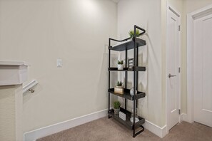 A hallway with a black metal shelf unit against the wall, holding decorative items and a sign. - 3BR townhouse near Disney | Pool & Mickey room (Clermont)