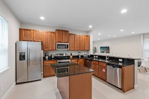 A modern kitchen with stainless steel appliances, wooden cabinets, and a central island. - 6BR near Disney | Private pool, spa & loft (Kissimmee)