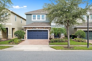 A residential building with a garage, a stone facade, and a well-maintained lawn. - 6BR near Disney | Private pool, spa & loft (Kissimmee)