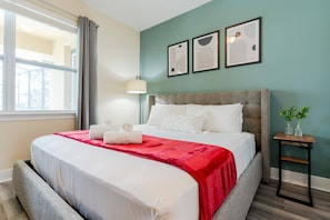 A hotel room with a bed, a nightstand, a lamp, and artwork on the wall. - 6BR near Disney | Private pool, spa & game room (Kissimmee)