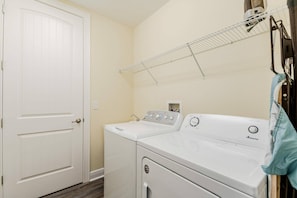 A laundry area with a front-loading washer and dryer, a white door, and a metal drying rack on the wall. - 6BR near Disney | Private pool, spa & game room (Kissimmee)