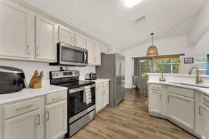 A modern kitchen with white cabinetry, stainless steel appliances, and a large window providing a view of the outdoors. - Terra Verde Oasis Private Pool (Kissimmee)