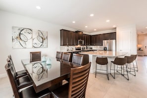 A modern kitchen with dark wood cabinets, stainless steel appliances, and a central island with bar stools. - 5BR near Disney | Pool, spa & 2 living rooms (Kissimmee)
