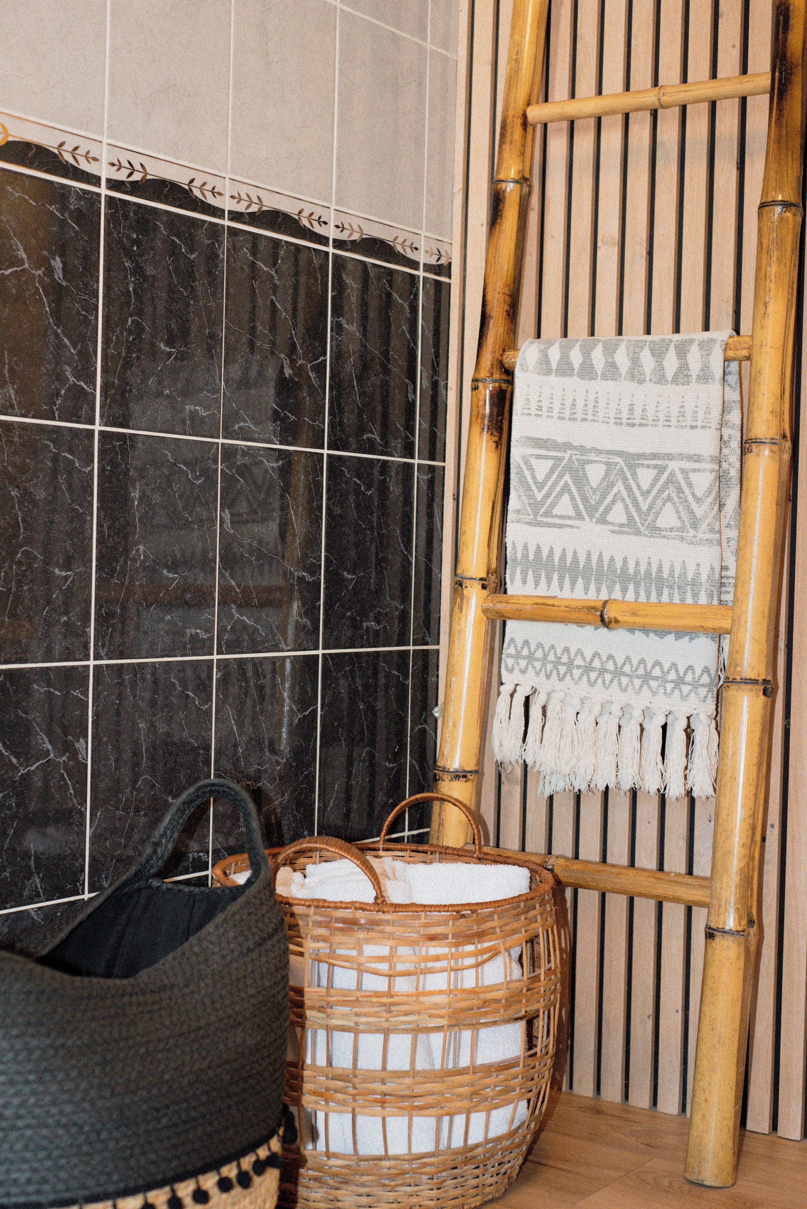 A bathroom with a black marble wall, a wooden chair with a towel, and a wicker basket.