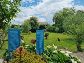 Un jardin avec une pelouse, une variété de plantes et, au fond, un bâtiment doté d’un toit en tuiles.