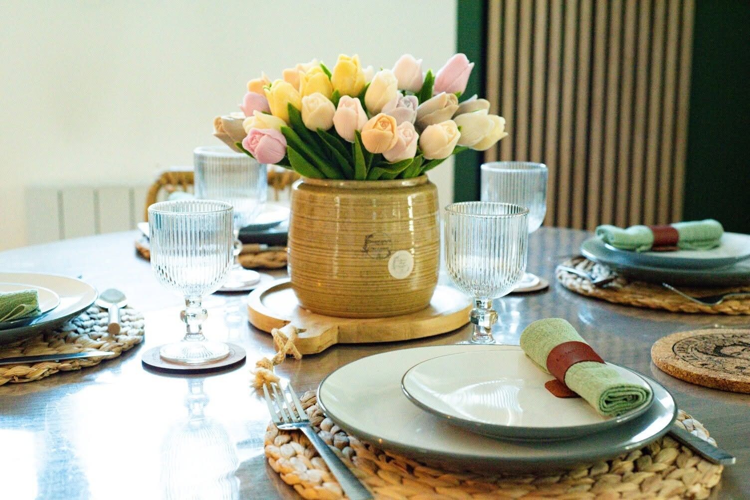 Una mesa de comedor dispuesta con platos, cubiertos y un jarrón de flores.