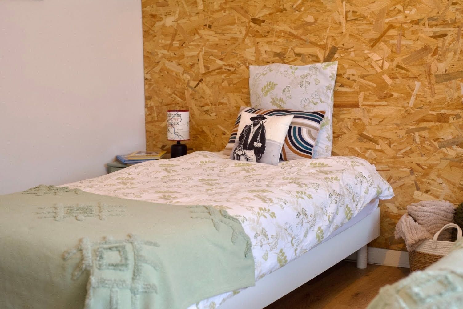 Une chambre à coucher avec un lit, des oreillers, une table de chevet, une lampe et un mur recouvert de copeaux de bois.