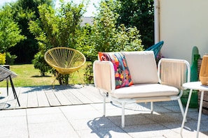 Une terrasse extérieure avec un canapé blanc, un fauteuil en osier et une petite table.