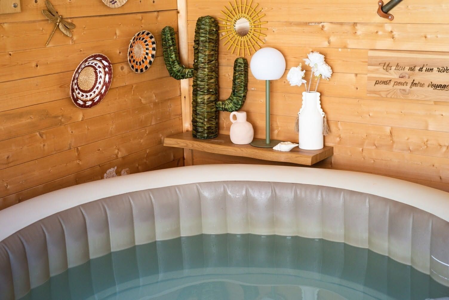 Un jacuzzi con un muro de madera al fondo, decorado con un cactus, un adorno de sol y una placa en la pared.