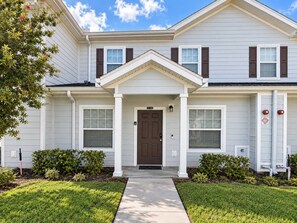 A two-story residential building with a front porch, a brown front door, and a mailbox. - 3BR townhome near Disney | Resort pool access (Kissimmee)