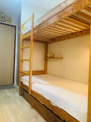 A bunk bed with a ladder, a shelf, and a door in a room with wooden flooring. - Vrbo Property (Tignes)