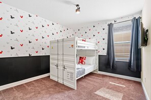 Een kamer met een stapelbed, een raam met luxaflex en een muur met Mickey Mouse stickers.